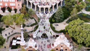 Aerial drone view of Park Guell. Antoni Gaudi architecture. A lot of greenery around, tourists - Starpik