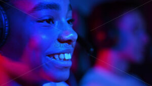 Black teen girl in headset playing video games in video game club with blue and red illumination, talking in voice chat. Slow motion - Starpik