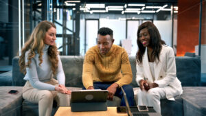 Multiracial group of people in an office discussing business while sitting on a sofa, tablet on the table - Starpik