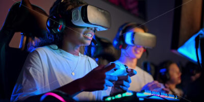 Premium stock video footage – White boy and black girl teens in VR headsets playing video games in video game club with blue illumination using a gamepad, virtual reality - Starpik Stock