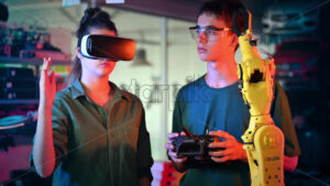 Teens doing experiments in robotics in a laboratory. Boy in protective glasses and girl in VR headset controlling the robot using controller and hand. Red and blue illumination. Slow motion - Starpik