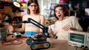 Two young happy engineers fixing a mechanical robot car in the workshop, using VR virtual reality headsets, computer programming - Starpik