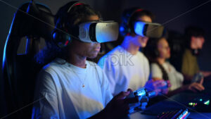 White boy and black girl teens in VR headsets playing video games in video game club with blue illumination using a gamepad, virtual reality - Starpik Stock