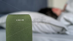 A sleeping woman turning off alarm clock on a portable wireless speaker with 4 luminous diodes - Starpik Stock