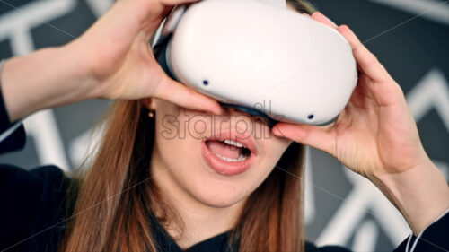 A young woman is excited while putting on VR glasses, controllers. Slow motion virtual reality - Starpik Stock