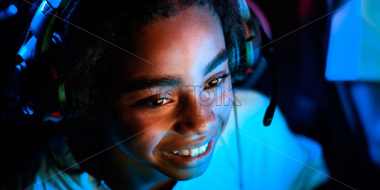 Black teen smiling girl in headset playing video games in video game club - Starpik