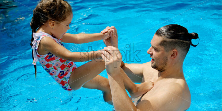 Father and daughter resting and swimming in a pool in summer - Starpik Stock