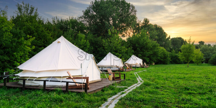 Glamping tents in nature with green grass at sunset. Summer season - Starpik Stock