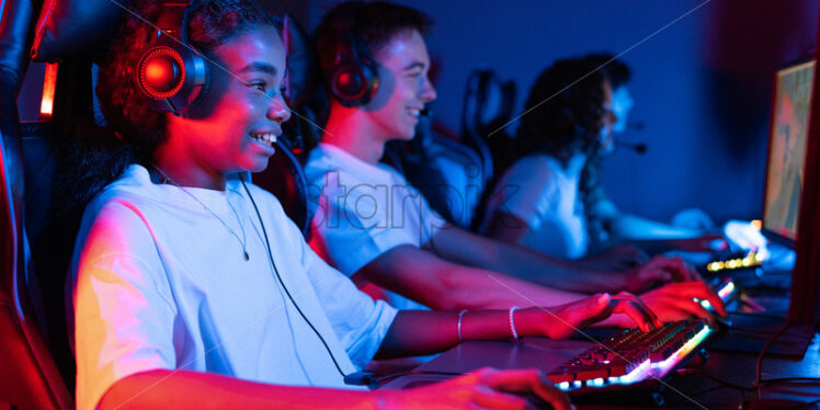 Group of multiracial teens in headsets playing video games in video game club with blue and red illumination. Keyboard and mouse with illumination - Starpik