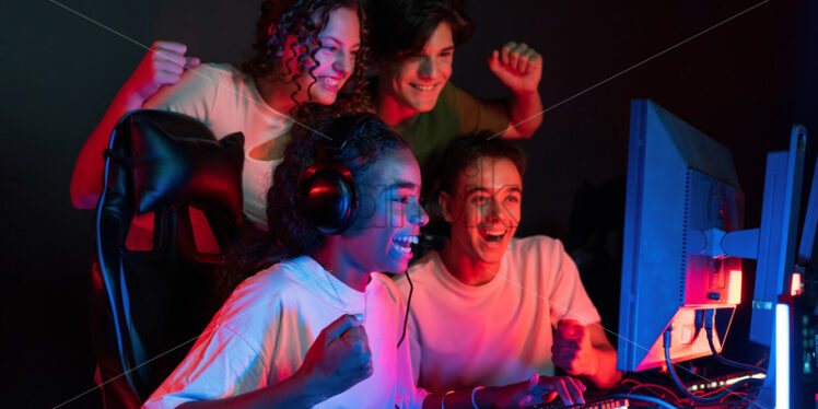 Group of multiracial teens playing video games in video game club with blue and red illumination. Excited because of a victory - Starpik