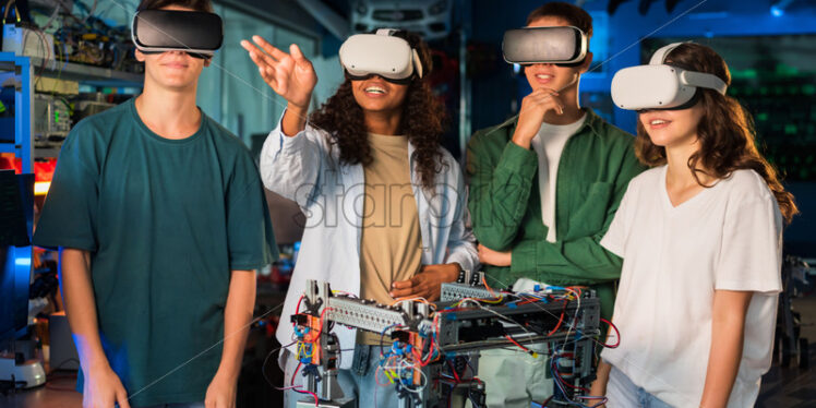 Group of young people in VR glasses doing experiments in robotics in a laboratory. Robot on the table - Starpik Stock