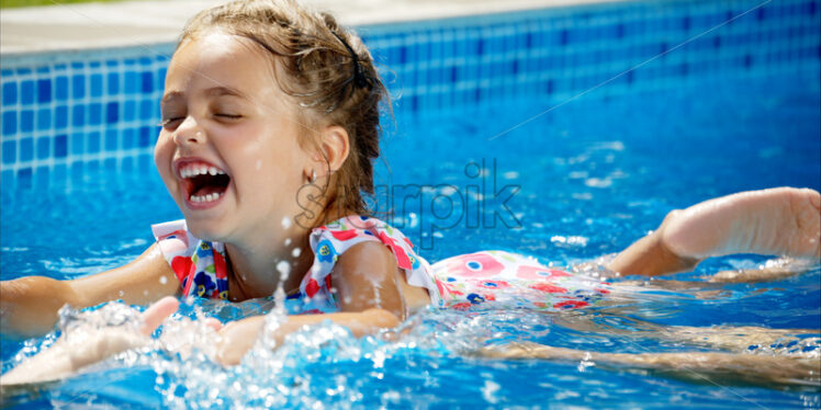 Little girl in sunglasses learning to swim in a pool with her mother - Starpik Stock