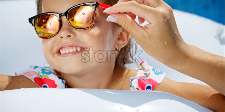Little girl in sunglasses resting on white pool balloon - Starpik Stock
