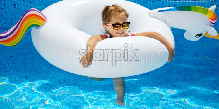Little girl in sunglasses resting on white pool balloon - Starpik Stock