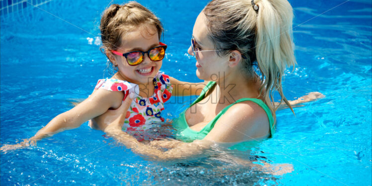 Mother and daughter resting and swimming in a pool in summer - Starpik Stock