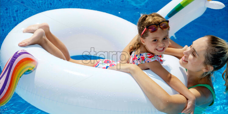 Mother and daughter resting and swimming in a pool in summer - Starpik Stock