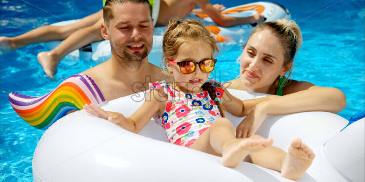 Mother with father and daughter resting and swimming in a pool in summer - Starpik Stock