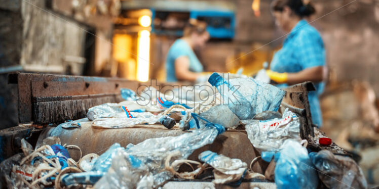 Plastic garbage on a conveyor belt at waste recycling factory. Workers on the background - Starpik Stock