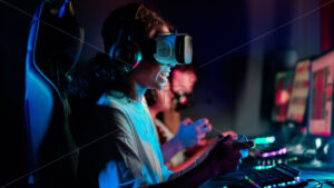 Premiu stock photo – Black teen smiling girl in VR headset playing video games using gamepad in video game club with blue illumination - Starpik