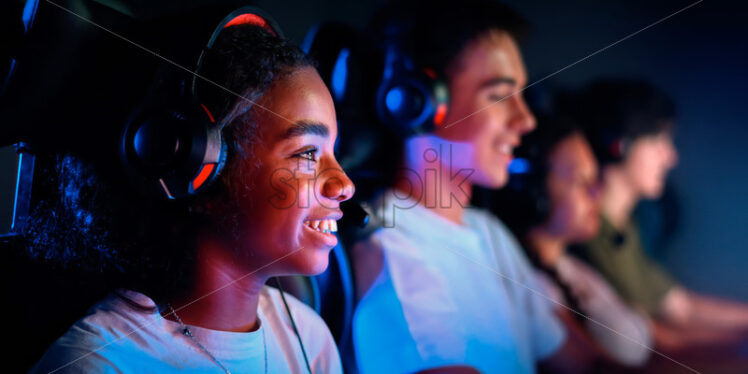 Premium stock photo – Multiracial group of teens in headsets playing video games in video game club with blue and red illumination. Keyboards and mice with illumination - Starpik