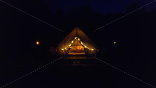 Tent with burning torches, lamps and wooden chairs at glamping, forest around, night - Starpik