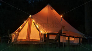 Tent with burning torches, lamps and wooden chairs at glamping, forest around, night - Starpik