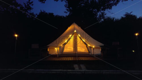 Tents with burning torches, lamps and wooden chairs at glamping, night - Starpik