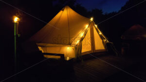 Tents with wooden chairs at glamping, lush forest around - Starpik