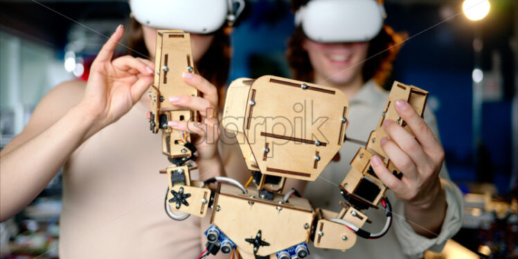 Two young engineers fixing a mechanical robot in the workshop, using VR virtual reality headsets - Starpik Stock
