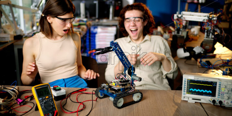 Two young happy engineers fixing a mechanical robot car in the workshop, using VR virtual reality headsets - Starpik Stock