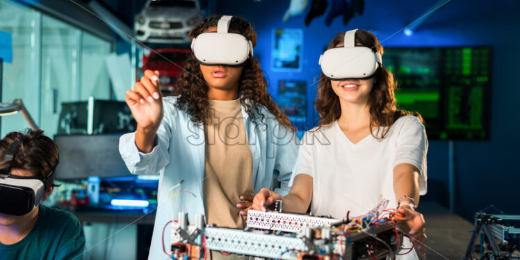Two young women in VR glasses doing experiments in robotics in a laboratory. Robot on the table - Starpik Stock