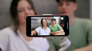 Young smiling man and woman blogger influencers talking and shooting themselves on smartphone on a stabiliser in a kitchen - Starpik Stock