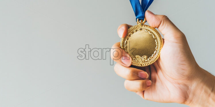 A hand holds a gold medal on a white background - Starpik Stock