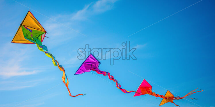 A series of colorful kites soaring high in the clear, blue sky - Starpik Stock