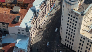 Aerial drone top view of a downtown road with moving traffic and walking people in sunlight. Bucharest, Romania - Starpik Stock