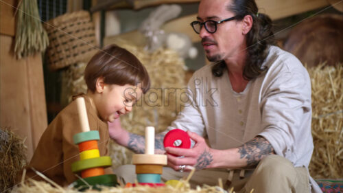 VIDEO Father playing with his son with colourful, ecological wooden toys in a barn, near square hay bales - Starpik