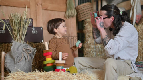 VIDEO Father playing with his son with colourful, ecological wooden toys in a barn, near square hay bales - Starpik