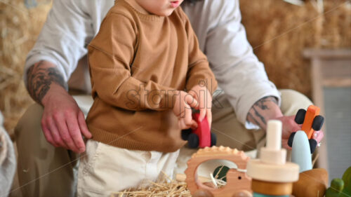 VIDEO Father playing with his son with colourful, ecological wooden toys in a barn, near square hay bales - Starpik