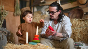 VIDEO Father playing with his son with colourful, ecological wooden toys in a barn, near square hay bales - Starpik