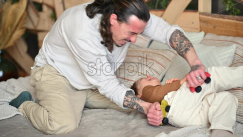 VIDEO Father playing with his son with colourful, ecological wooden toys on the bed - Starpik