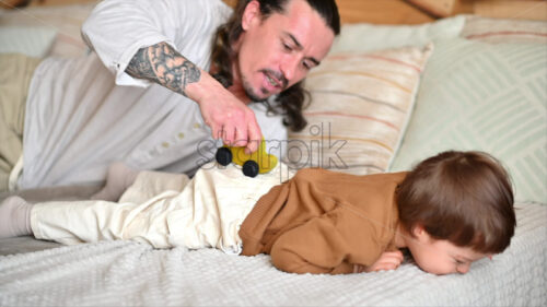 VIDEO Father playing with his son with colourful, ecological wooden toys on the bed - Starpik