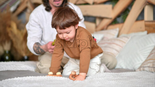 VIDEO Father playing with his son with colourful, ecological wooden toys on the bed - Starpik