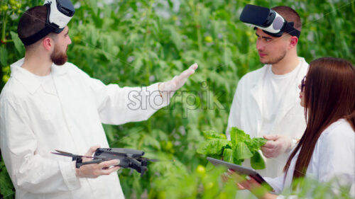 VIDEO Three laboratory technicians in white coats wearing Virtual Reality headsets, holding a drone and a tablet, analysing lettuce grown with the Hydroponic method in a greenhouse - Starpik