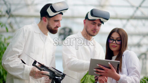 VIDEO Three laboratory technicians in white coats wearing Virtual Reality headsets, holding a drone and a tablet, analysing lettuce grown with the Hydroponic method in a greenhouse - Starpik