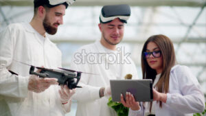 VIDEO Three laboratory technicians in white coats wearing Virtual Reality headsets, holding a drone and a tablet, analysing lettuce grown with the Hydroponic method in a greenhouse - Starpik