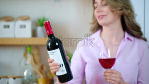 VIDEO Woman holding a glass and a bottle of red wine in the kitchen - Starpik