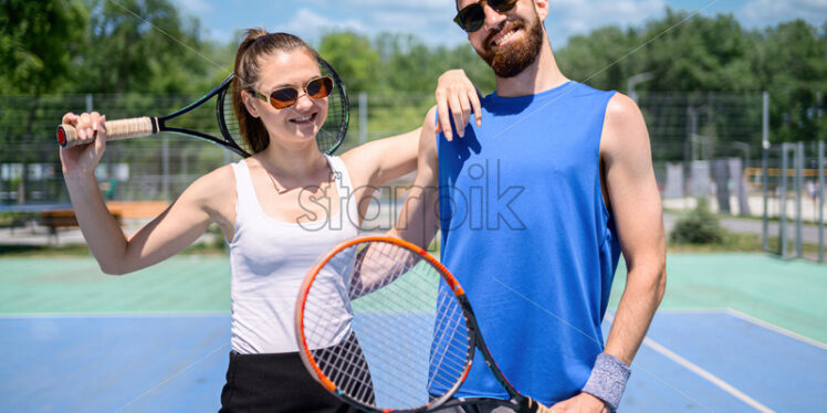 Portrait of a happy young couple holding tennis rackets - Starpik