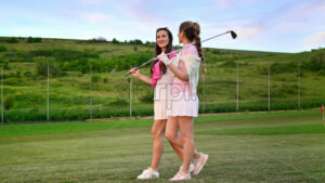 VIDEO Chisinau, Moldova – June 07, 2024: Two women dressed in white and pink clothes, with golf clubs on their shoulders, walking and talking on the golf course - Starpik