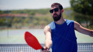VIDEO Close up of a man in a blue shirt playing pickleball with a red racket on a sunny day - Starpik