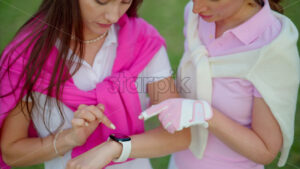 VIDEO Close up of two women dressed in white and pink clothes touching a smart watch on the golf course - Starpik